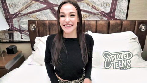Smiling Asian teen with long dark hair in black top, teasing on bed