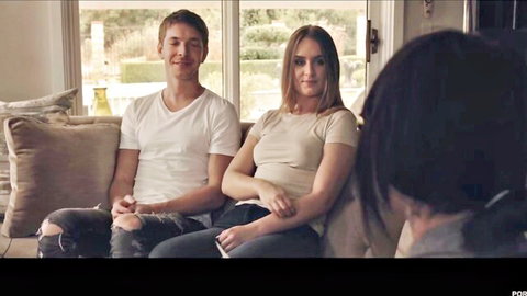 Handsome guy smiles with sexy brunette babe on couch as black-haired hottie faces away teasing threesome vibe