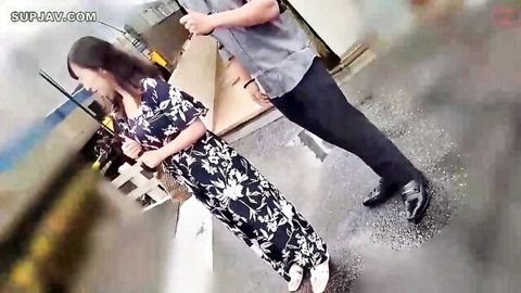 Amateur Asian wife in floral dress smiles back at man holding bag outdoors