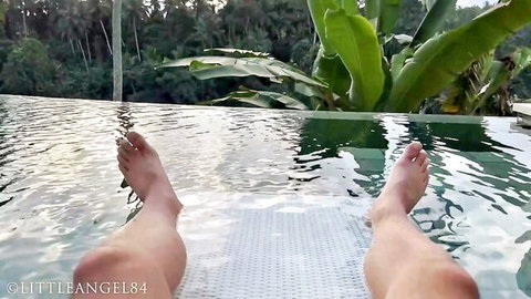 Sexy bare feet with red polish and toned legs dangling in infinity pool water