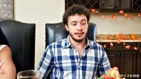 Smiling curly-haired guy in plaid shirt sits with hot woman at Halloween kitchen table