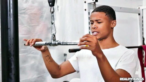 Muscular black stud with tattoos gripping pull-up bar in gym workout