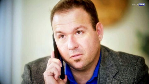 Middle-aged man in gray suit and blue shirt talking intently on black phone