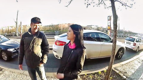 Smiling Asian couple flirting by white sedan on sunny street
