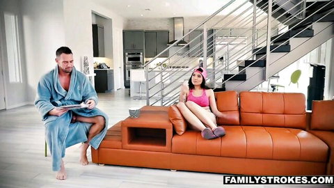 Brenna Sparks in pink top and shorts lounging on couch with robed stepdad