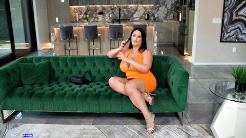 Sarah Arab in tight orange dress, teasing with cleavage on couch
