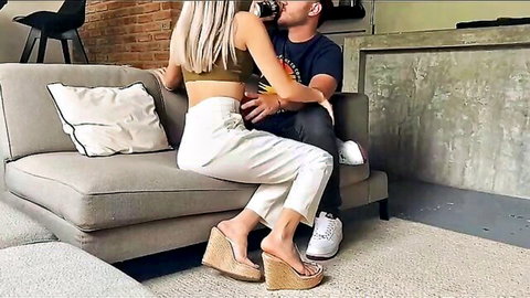 Petite blonde in crop top and white pants straddling guy passionately kissing on couch