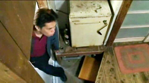 Japanese man in maroon jacket stands in rustic kitchen near old white fridge