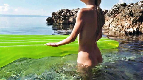Blonde Nancy A nude in shallow water with pool floatie