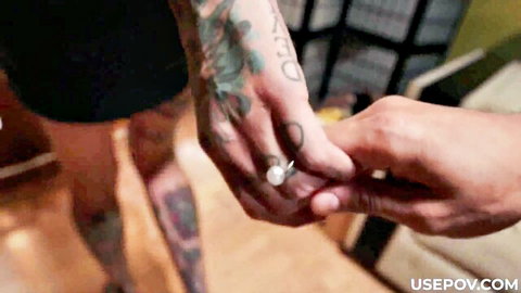 Tattooed man's hand intimately gripping woman's pearl-ringed fingers closeup