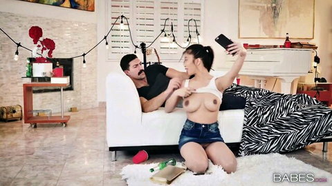 Topless Asian with big natural tits kneels grabbing DILF's crotch bulge taking selfie