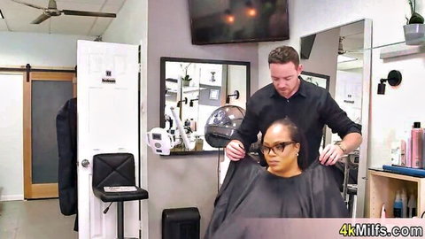 Bridgette B oversees salon stylist with ebony client under cape