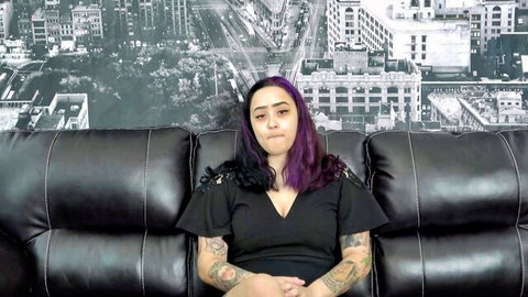 Indigo Dances in black lace dress, tattoos, purple hair on couch