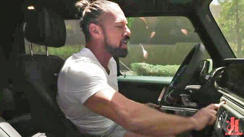 Intense bearded man with ponytail driving Jeep in white tank top