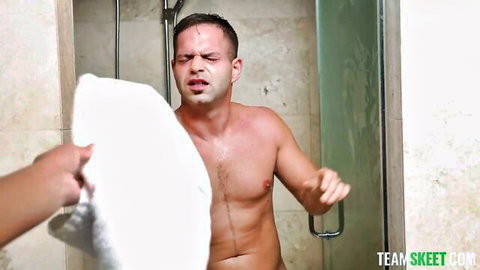 Muscular naked man grimacing in steamy shower as hand holds towel over his cock