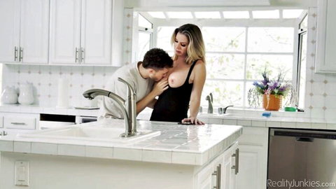 Blonde MILF with massive fake tits gets her breasts sucked by guy in kitchen