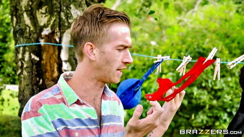 Skinny guy in striped shirt holding blue ball and red clips on outdoor clothesline in Brazzers scene