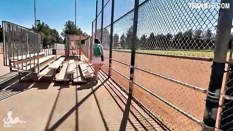 Skinny long-haired brunette walks away exposing bare ass cheeks in tiny shorts at public baseball field