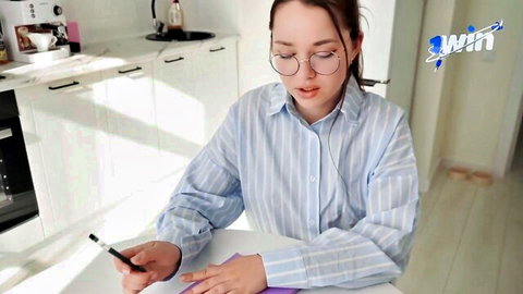 Brunette with glasses in striped shirt writing on paper at kitchen table