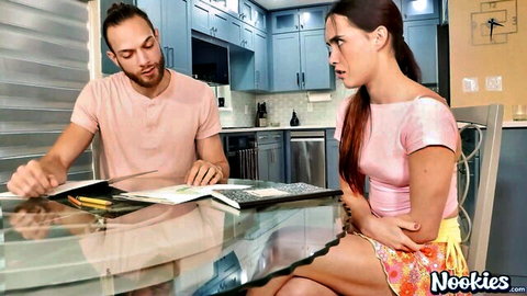 Skinny brunette teen in pink top and mini skirt glares angrily at guy reading magazine at kitchen table