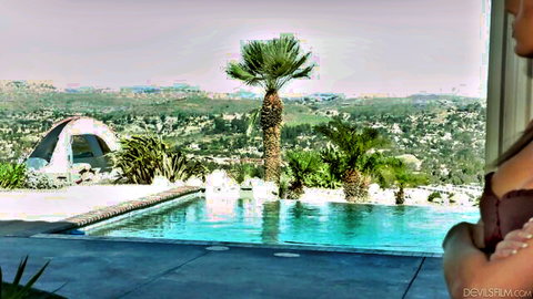Brunette beauty arms crossed by turquoise infinity pool overlooking palm trees and hills
