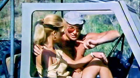 Tanned blonde ponytail babe hugs shirtless stud pointing finger in vintage jeep car