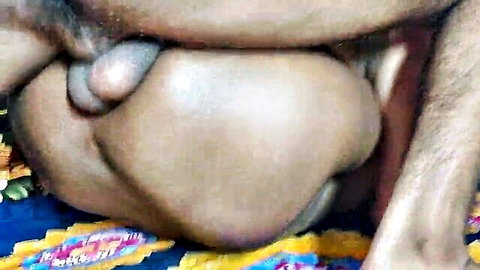 Close-up of thick hairy brown cock and heavy balls hanging between dark thighs on colorful bedspread