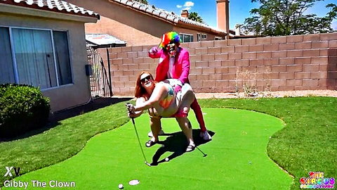 Julie Ginger in bikini with Gibby The Clown in doggy pose on mini golf green
