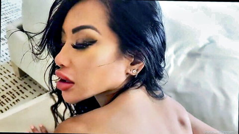 Seductive Asian brunette babe with plump red lips and smokey eyes poses topless in hotel bed