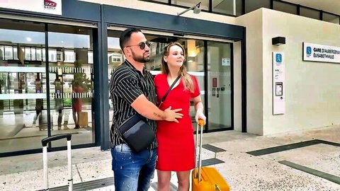 Cat In Mini and partner smile outside clinic with luggage, red dress embrace