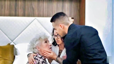 86-year-old granny embraced by young couple on bed in intimate scene