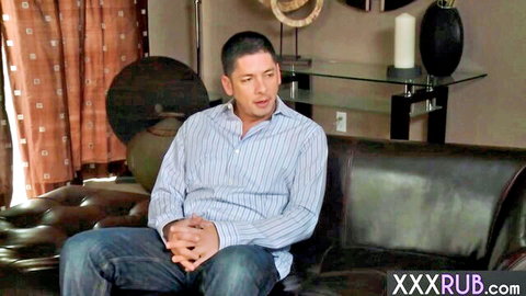Handsome man in striped shirt and jeans sits on black leather couch in living room ready for massage.