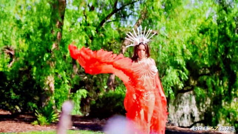 Sexy brunette in skimpy red feather outfit and headdress posing seductively in lush forest
