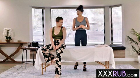 Curvy brunette MILF stands over young brunette in green bralette during lesbian massage tease
