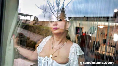 Sexy mature granny in white lace lingerie poses seductively by window