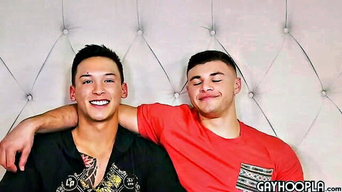 Two hot gay twinks smiling with arm around shoulder on bed
