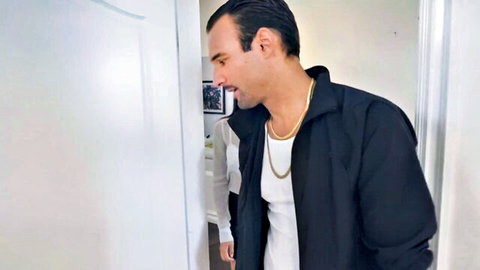 Handsome olive-skinned man in black jacket smirking sideways in office doorway