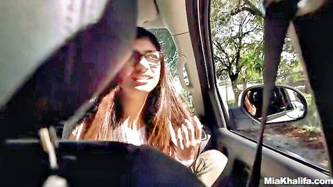 Smiling brunette Mia Khalifa in glasses waving from car passenger seat
