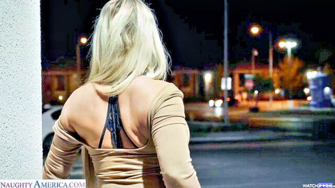 Blonde in sexy backless top teasing curves against night street wall
