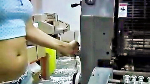 Sexy Asian woman in polka-dot crop top exposing midriff, operating industrial machine
