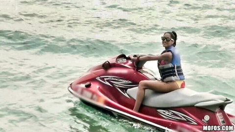 Chloe Amour in bikini riding red jet ski on clear water, sexy outdoor vibe