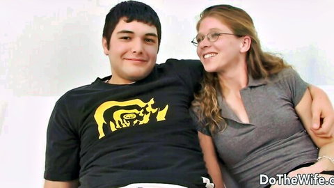 Freckled wife in glasses smiles hugging young man on couch before cuckold fuck