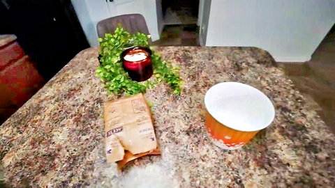 Spilled white powder from torn paper bag next to orange cup on kitchen table