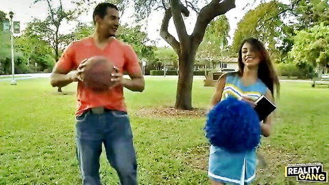 Sexy Latina cheerleader in tight uniform flirts with muscular guy holding basketball outdoors