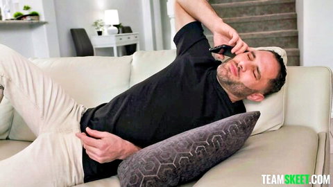 Bearded man lounging sideways on couch talking on phone in living room