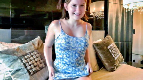 Cute smiling brunette teen in short floral spaghetti strap dress teasing cleavage on bed