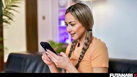 Veronica Leal blonde with pigtails, smiling seductively holding phone in orange top