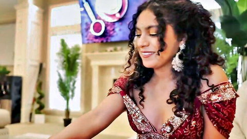 Curvy South Asian woman with curly hair smiling in revealing red embroidered off-shoulder dress showing deep cleavage