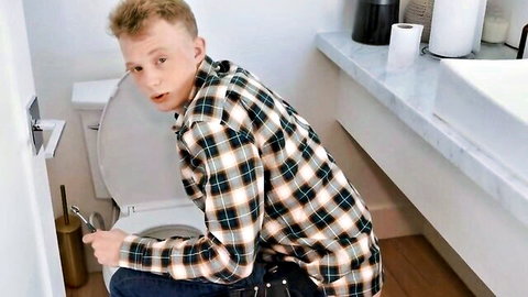 Surprised young man on toilet holding plunger in bathroom