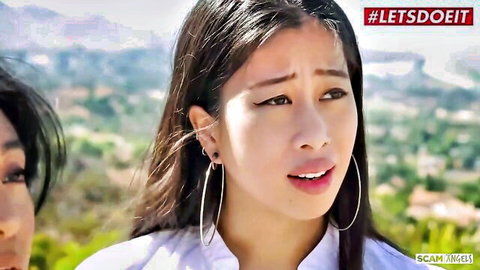 Young Asian beauty with long hair and hoop earrings in white top looks surprised outdoors